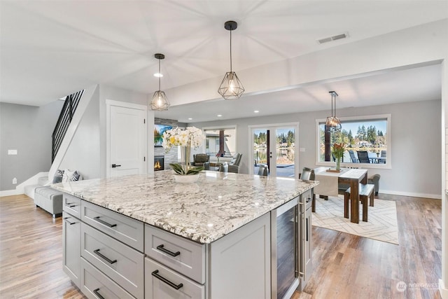 kitchen featuring pendant lighting, light stone countertops, light hardwood / wood-style floors, and wine cooler