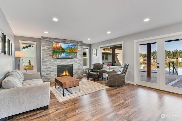 living room featuring hardwood / wood-style flooring, a water view, a stone fireplace, and french doors