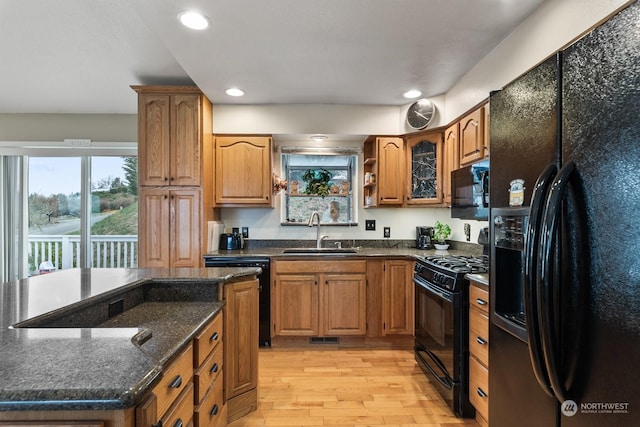 kitchen featuring dark stone counters, light hardwood / wood-style floors, sink, and black appliances