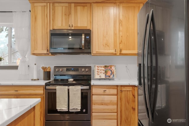 kitchen featuring black fridge, light brown cabinets, light stone counters, and electric stove