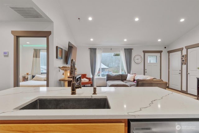 kitchen featuring stainless steel dishwasher, vaulted ceiling, sink, and light stone counters