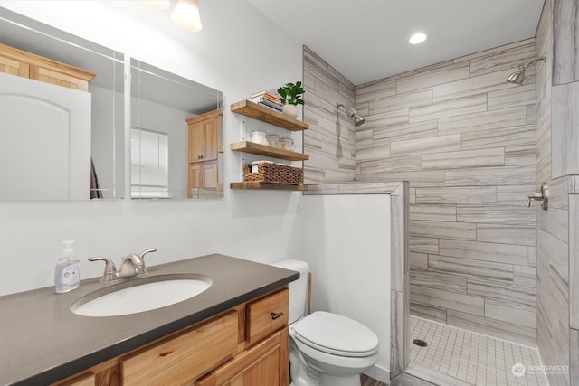 bathroom featuring toilet, a tile shower, and vanity