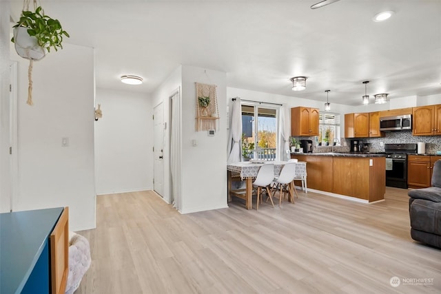 kitchen with light hardwood / wood-style floors, kitchen peninsula, appliances with stainless steel finishes, decorative backsplash, and hanging light fixtures