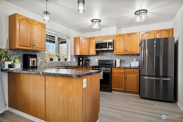 kitchen featuring kitchen peninsula, appliances with stainless steel finishes, decorative light fixtures, light wood-type flooring, and sink