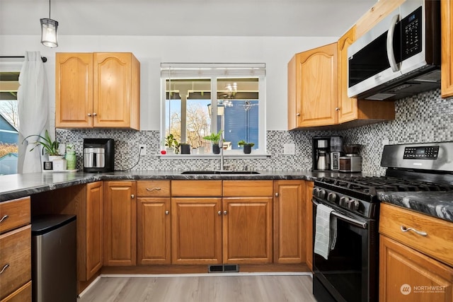 kitchen featuring pendant lighting, appliances with stainless steel finishes, decorative backsplash, sink, and light hardwood / wood-style flooring