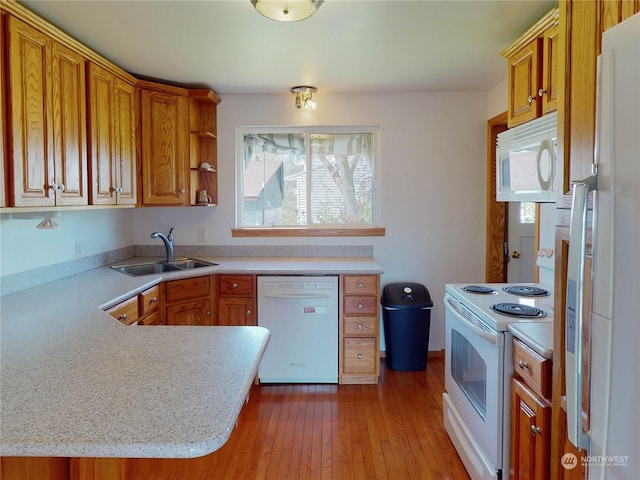 kitchen with kitchen peninsula, sink, white appliances, and light hardwood / wood-style flooring