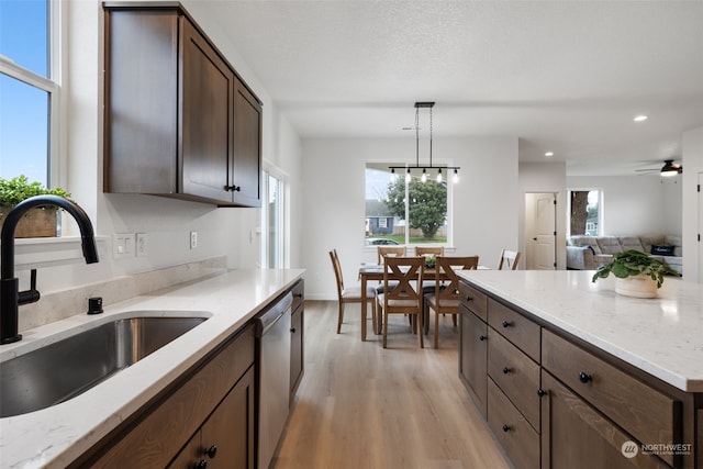 kitchen with light stone counters, sink, hanging light fixtures, and dishwasher