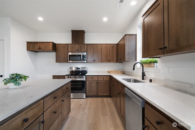 kitchen featuring dark brown cabinetry, stainless steel appliances, sink, light stone counters, and light hardwood / wood-style flooring