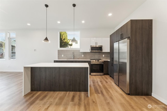 kitchen featuring pendant lighting, light wood-type flooring, white cabinetry, stainless steel appliances, and dark brown cabinetry