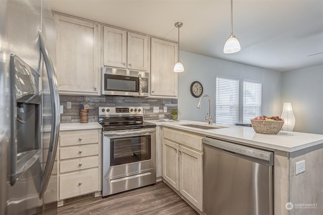 kitchen featuring pendant lighting, sink, appliances with stainless steel finishes, backsplash, and kitchen peninsula