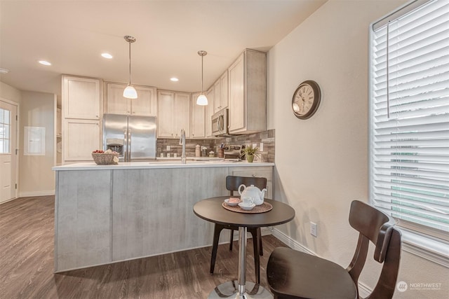 kitchen with dark wood-type flooring, tasteful backsplash, decorative light fixtures, kitchen peninsula, and stainless steel appliances