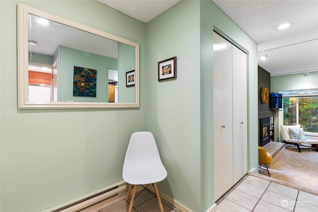 hallway with a baseboard radiator, a textured ceiling, rail lighting, and light colored carpet