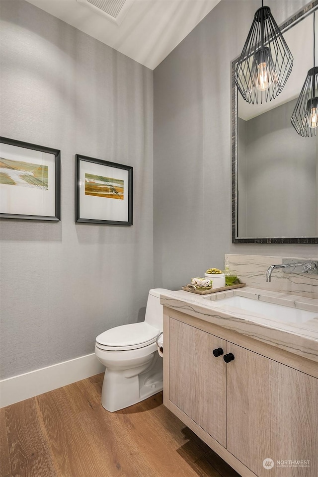 bathroom with an inviting chandelier, wood-type flooring, toilet, and vanity