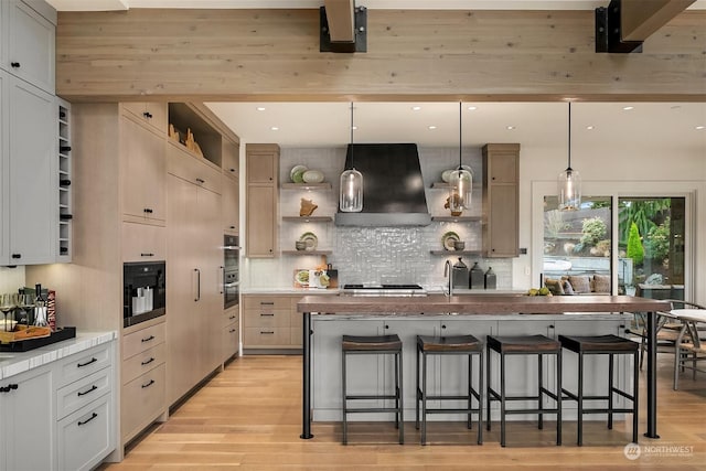 kitchen featuring a kitchen breakfast bar, decorative light fixtures, a kitchen island with sink, and wall chimney range hood