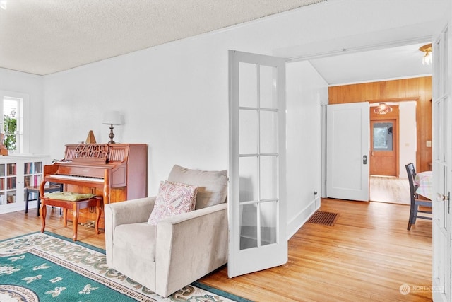 sitting room with wood-type flooring, a textured ceiling, french doors, and wooden walls