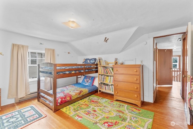 bedroom featuring a baseboard heating unit, light wood-type flooring, and vaulted ceiling