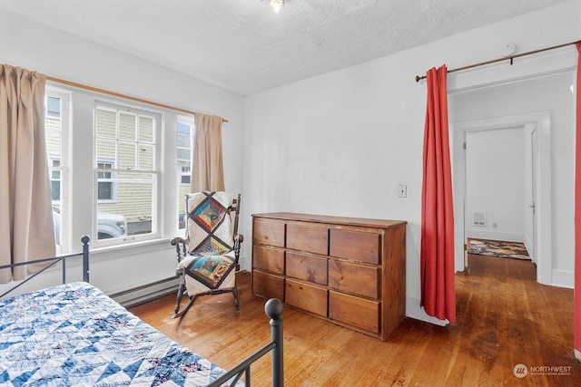 bedroom featuring hardwood / wood-style floors, a textured ceiling, and a baseboard heating unit