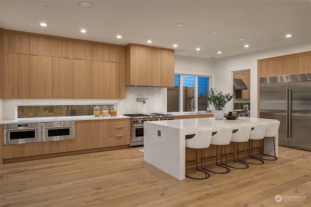 kitchen with a center island, a kitchen bar, light hardwood / wood-style floors, premium appliances, and tasteful backsplash