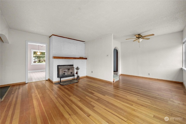 unfurnished living room featuring ceiling fan, a wood stove, a textured ceiling, and light hardwood / wood-style flooring