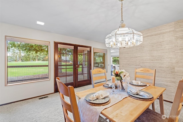 dining area with a healthy amount of sunlight, french doors, light colored carpet, and a chandelier