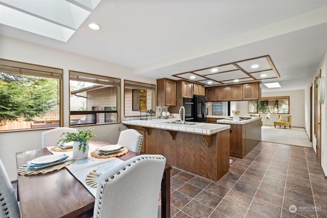 kitchen featuring tile counters, a skylight, sink, black fridge, and kitchen peninsula