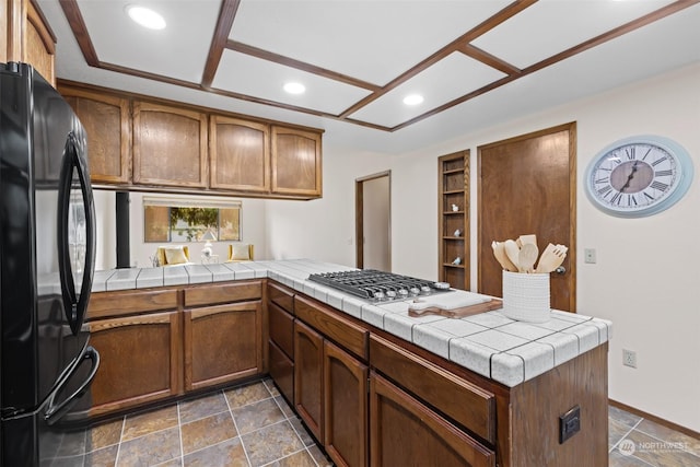 kitchen with stainless steel gas stovetop, tile counters, kitchen peninsula, and black refrigerator