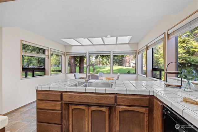 kitchen with a skylight, tile counters, and sink