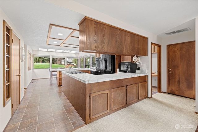 kitchen featuring light carpet, tile countertops, kitchen peninsula, and black appliances