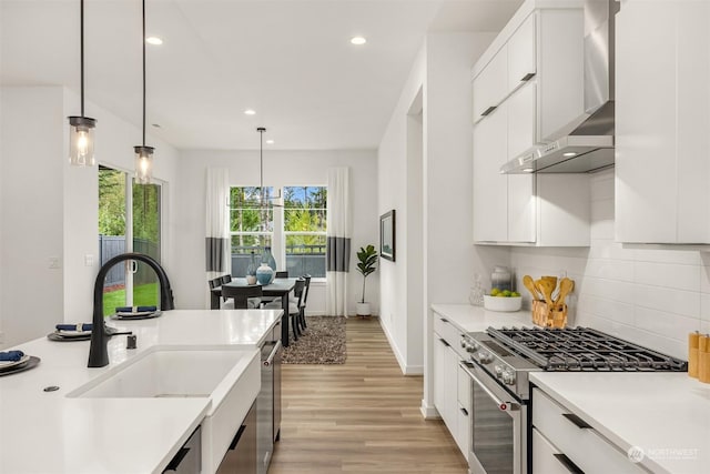 kitchen with white cabinets, wall chimney exhaust hood, stainless steel appliances, light hardwood / wood-style floors, and hanging light fixtures