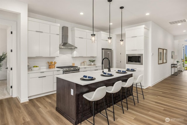 kitchen featuring hardwood / wood-style floors, an island with sink, white cabinets, wall chimney exhaust hood, and high quality appliances