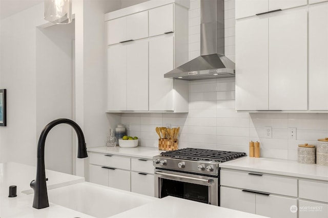 kitchen with sink, white cabinetry, wall chimney exhaust hood, and stainless steel gas range oven