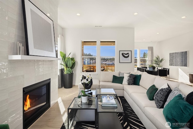 living room with wood finished floors, a glass covered fireplace, visible vents, and recessed lighting