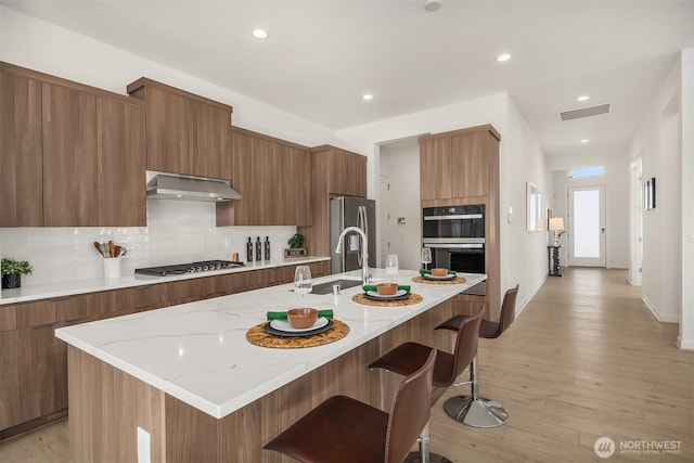 kitchen with under cabinet range hood, modern cabinets, visible vents, and stainless steel appliances