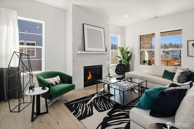 living room with light wood finished floors, visible vents, a tiled fireplace, and recessed lighting