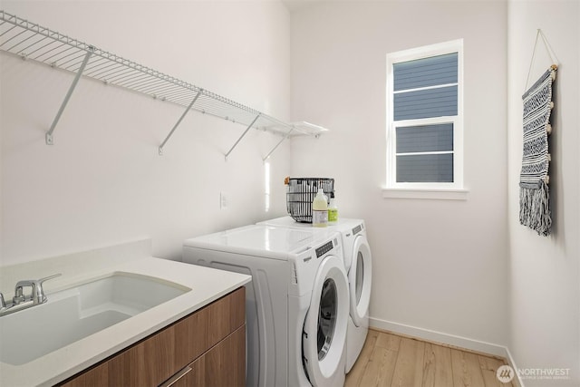 laundry area with a sink, baseboards, light wood-style floors, independent washer and dryer, and cabinet space