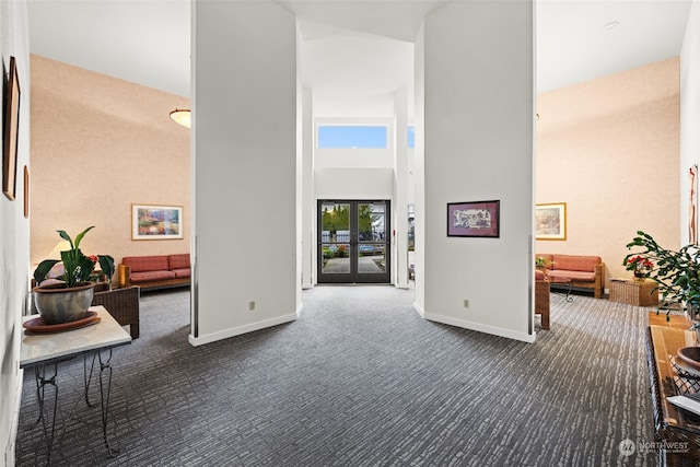 hall featuring a towering ceiling and dark carpet