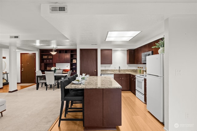 kitchen with light carpet, white appliances, a kitchen island, a breakfast bar, and sink