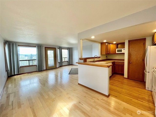 kitchen with butcher block counters, kitchen peninsula, white appliances, light hardwood / wood-style flooring, and sink