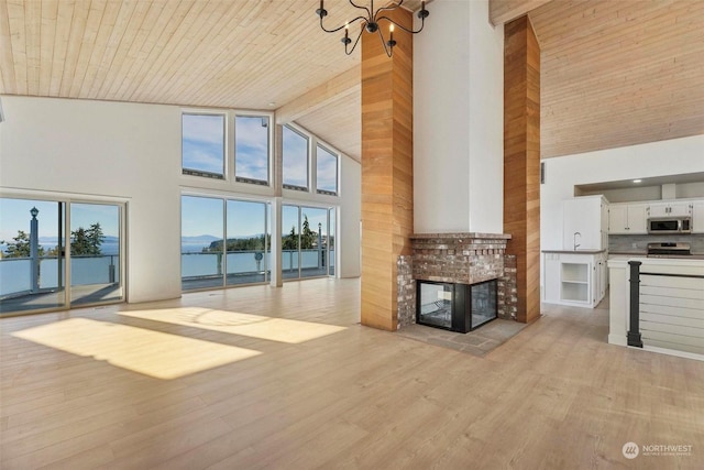 unfurnished living room with a water view, wood ceiling, high vaulted ceiling, a fireplace, and light hardwood / wood-style floors