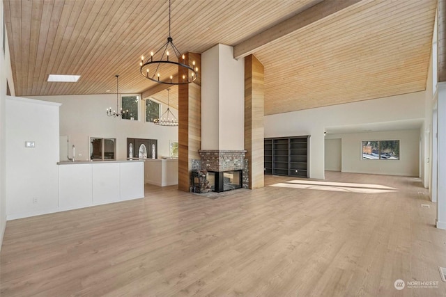 unfurnished living room featuring beam ceiling, a multi sided fireplace, wooden ceiling, a chandelier, and light wood-type flooring