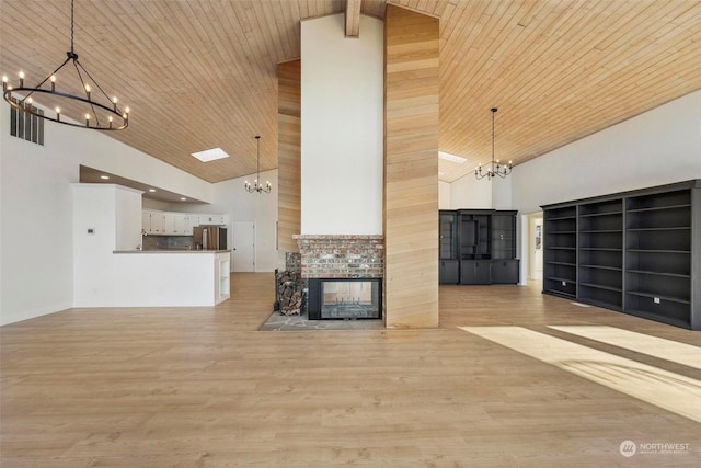 unfurnished living room featuring a notable chandelier, light hardwood / wood-style floors, high vaulted ceiling, and a multi sided fireplace