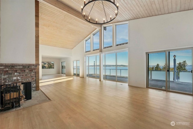 unfurnished living room with light hardwood / wood-style flooring, a water view, a healthy amount of sunlight, a brick fireplace, and a chandelier