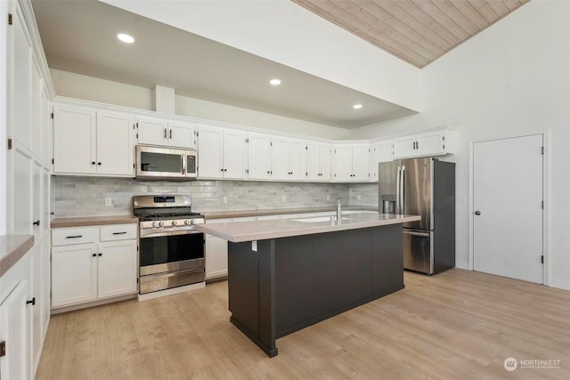 kitchen featuring stainless steel appliances, an island with sink, white cabinets, and light wood-type flooring