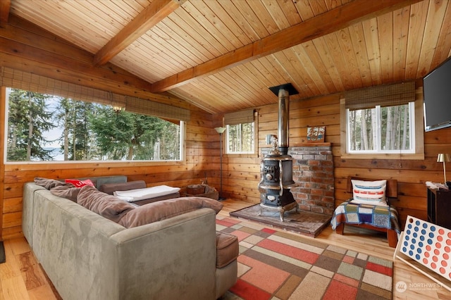 living room with light wood-type flooring, a wood stove, plenty of natural light, and lofted ceiling with beams