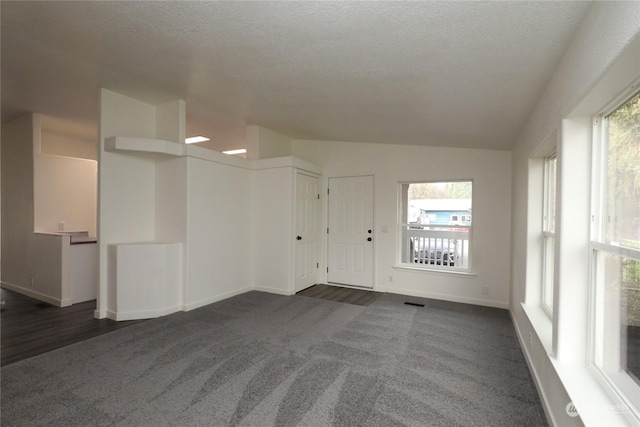 spare room featuring a textured ceiling, dark colored carpet, and vaulted ceiling