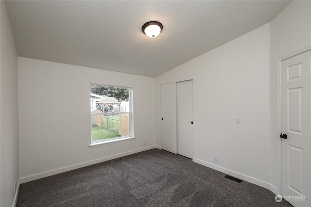 unfurnished bedroom with a closet, vaulted ceiling, a textured ceiling, and dark colored carpet