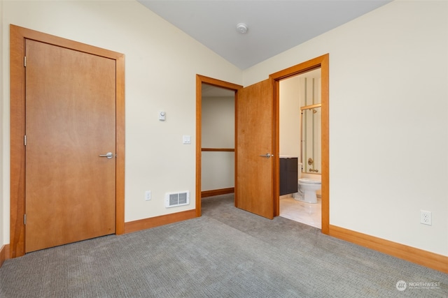 unfurnished bedroom with light colored carpet, a closet, ensuite bath, and vaulted ceiling