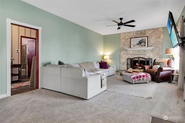 carpeted living room with ceiling fan and a stone fireplace