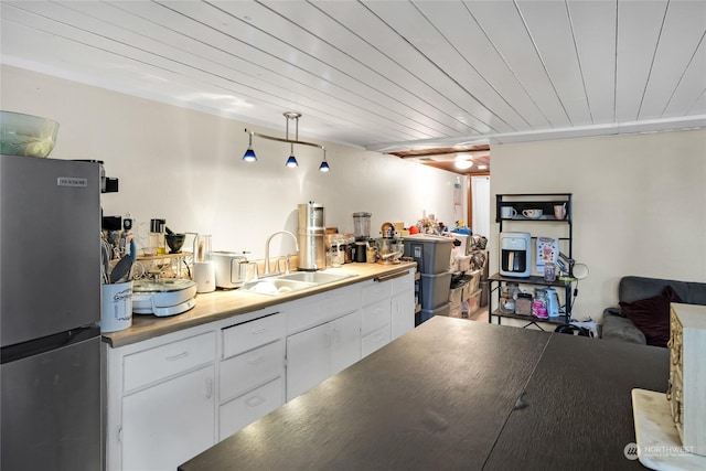 kitchen with stainless steel refrigerator, white cabinets, sink, and wooden ceiling