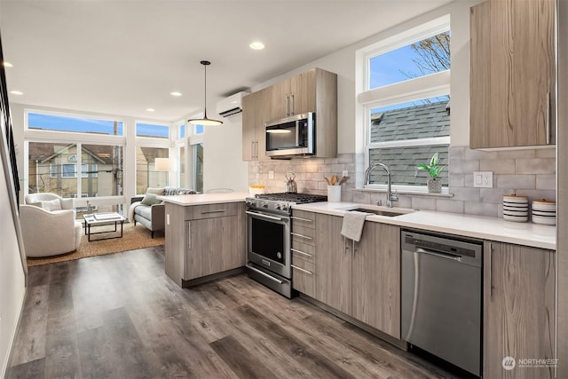 kitchen featuring kitchen peninsula, stainless steel appliances, a wall mounted air conditioner, decorative light fixtures, and sink